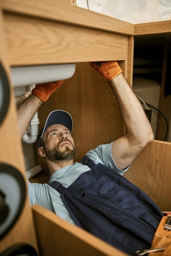 A plumber lying under a kitchen sink repairing the drain pipes